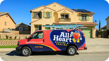 A red and blue All Heart Heating & Cooling van is parked on a residential street in front of a beige two-story house with solar panels.